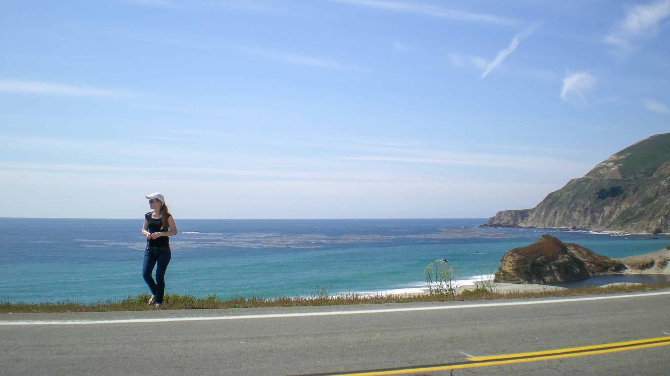 Pacific Coast Highway Road Trip, photo of Erin crossing the Pacific Coast Highway with panoramic views .