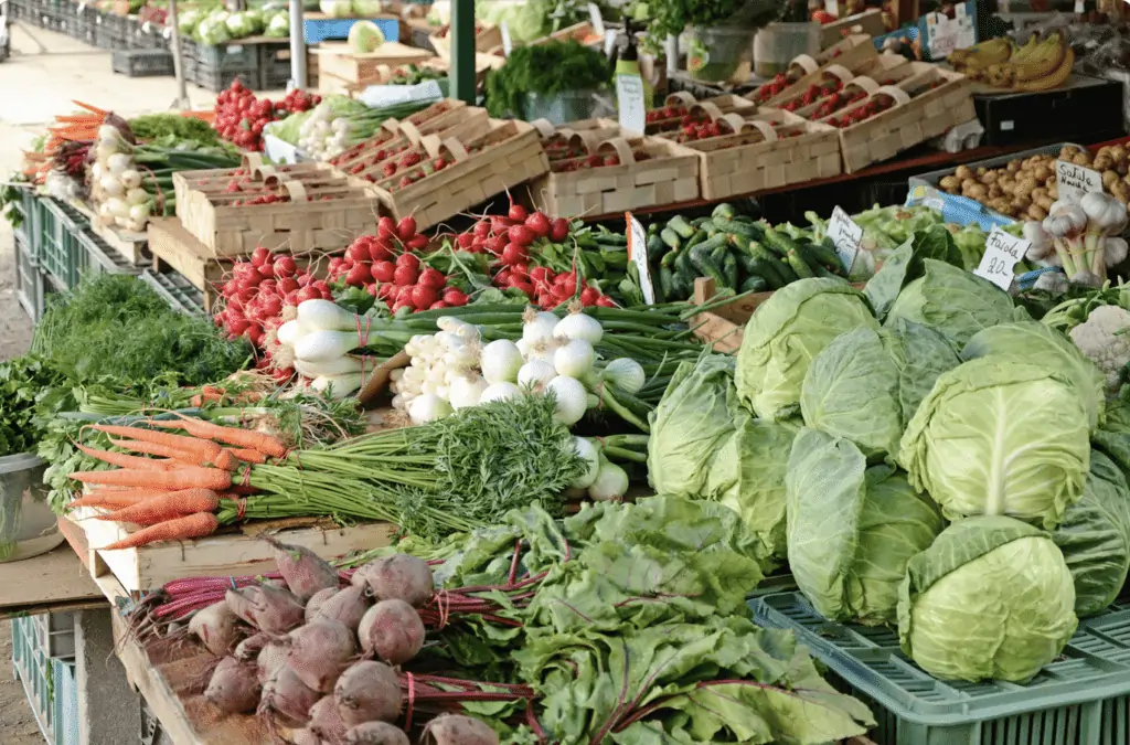 Canva  photo of cabbage, carrots, and a variety of fresh produce at the farmer's market.