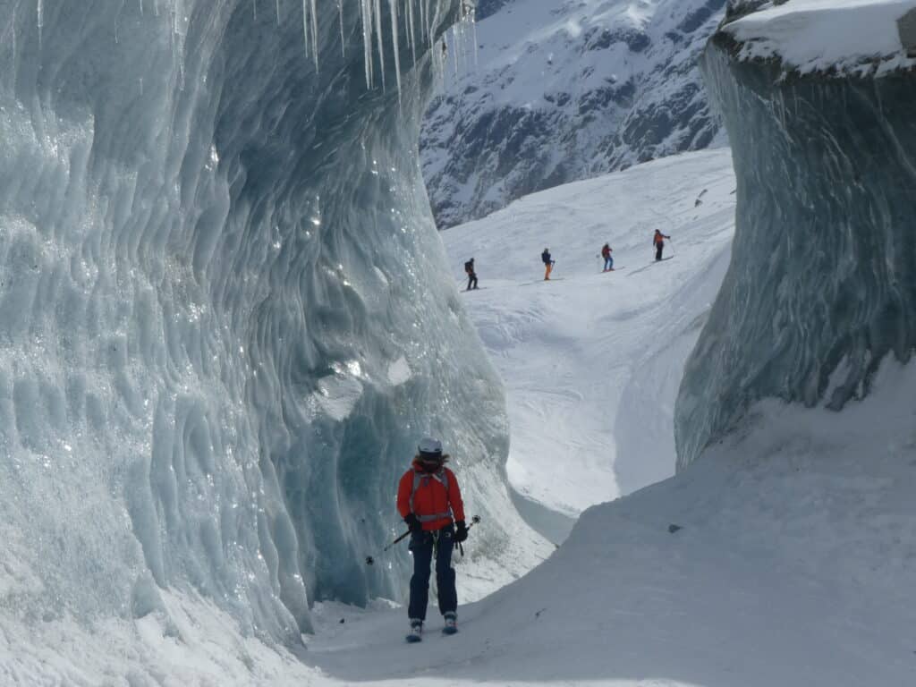 Tom's Chamonix Snowboarding off-piste adventure.  Photo provided by Tom.  Shows him snowboarding through an ice tunnel with others skiing in the distance.