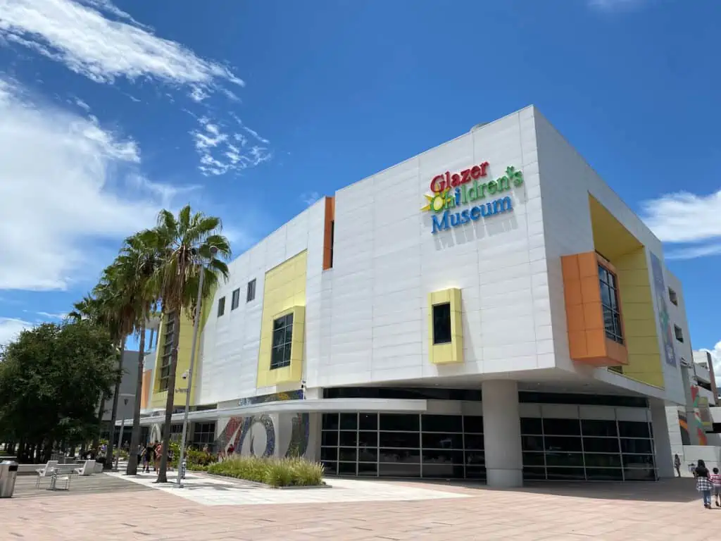 Exterior photo of Glazer Children's Museum in Tampa.  It has a playground in the distance by the riverwalk.
