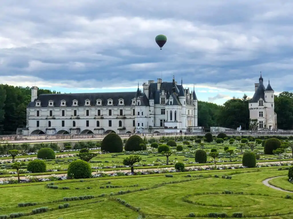 Chateau de Chenonceau at dusk with a hot air balloon flying over it.  The photo shows the gardens in the front of the photo.  