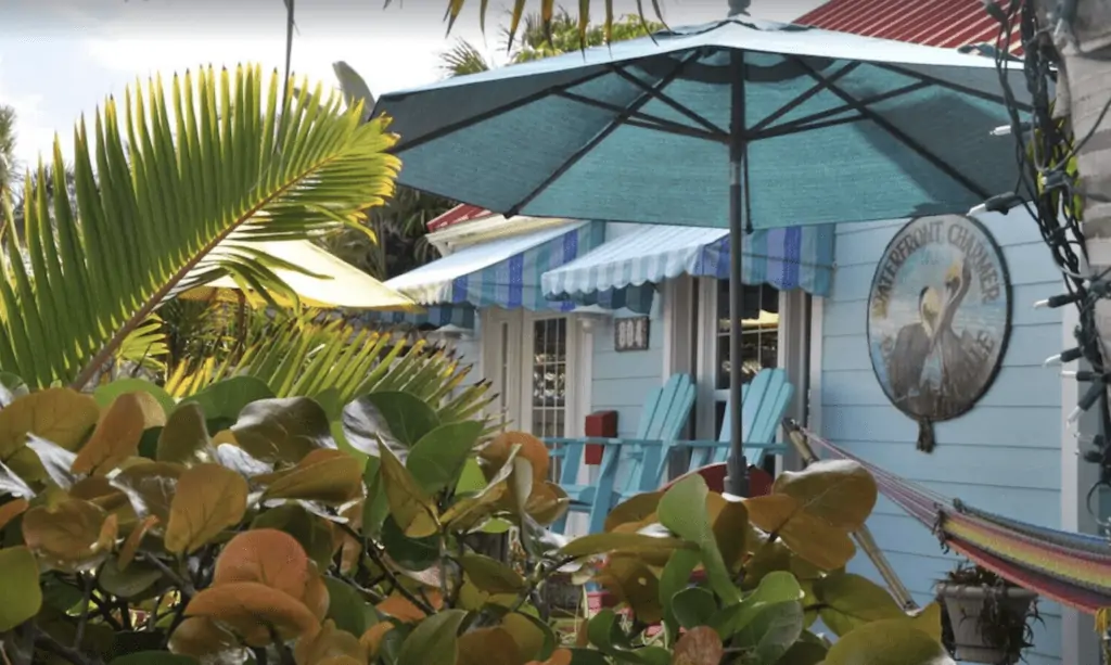 VRBO Pass-a-Grille Rentals, photo of the outside of the waterfront charmer house with a soft pastel blue exterior, sea grapes, and beach umbrella and chairs.