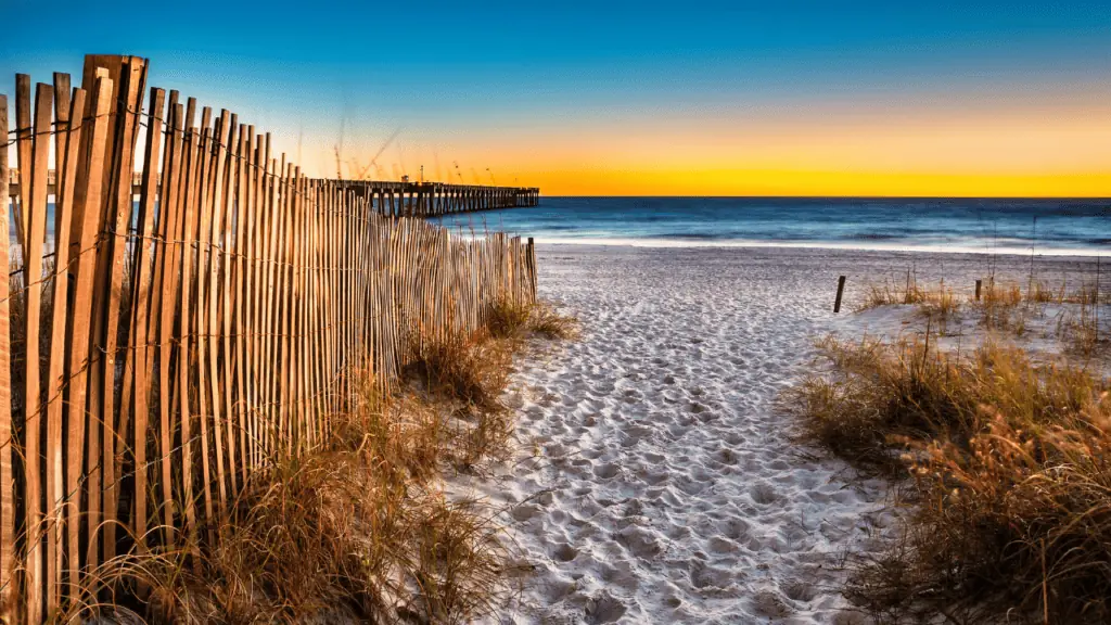 Panama city Beach view of the pier in the distance at sunset with white sandy beaches and a wooden fence