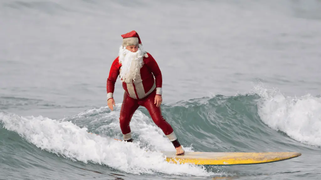 Surfing santa on a surf board in the water.